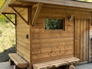 Una cabaña de madera con un banco, una puerta y una ventana.