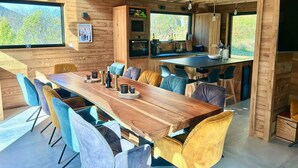 Un interior de madera con una larga mesa de comedor, sillas coloridas y una zona de cocina con pileta y horno.