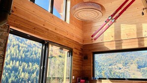 Una cabaña de madera con amplias ventanas que ofrecen vistas de una zona montañosa boscosa.