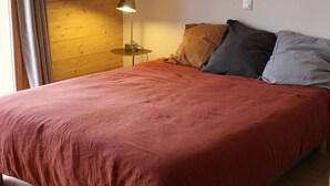 Een bed met een rode sprei, een lamp op een nachtkastje, en een houten wand.