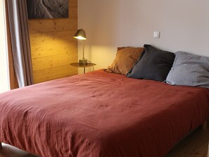 A bed with a red bedspread, a lamp on a bedside table, and a wooden wall. - Central apartment 2 rooms, Arâches, 5 guests, parking, wifi (Arâches-la-Frasse)
