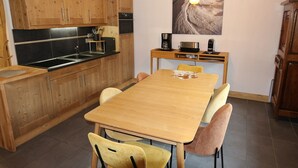 Een moderne keuken met houten kastjes, een zwart aanrecht en een eethoek met een houten tafel en gele stoelen.