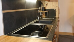 Een keuken met een zwart betegelde spatwand, roestvrijstalen apparatuur, houten kastjes en een zwart aanrecht.