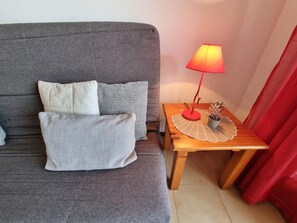 A grey sofa with three pillows, a small wooden side table with a red lamp, and a potted plant. - Apartment in L'Escala with terrace near the beach (L'Escala)