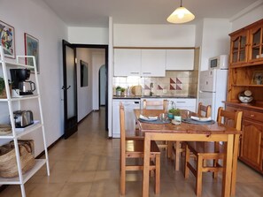 A modern kitchen with white cabinets, a wooden dining table set for four, and a coffee machine. - Apartment in L'Escala with terrace near the beach (L'Escala)