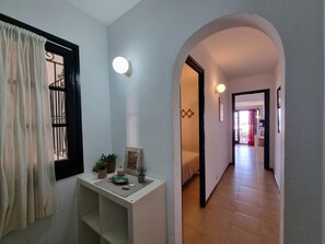 A hallway with a white wall, a small table with decorative items, a window with curtains, and a door leading to another room. - Apartment in L'Escala with terrace near the beach (L'Escala)