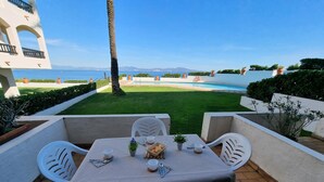 A patio with a table set for two, overlooking a swimming pool and a grassy area with potted plants. - Apartment in L'Escala with terrace near the beach (L'Escala)