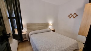 A small, neatly arranged bedroom with a bed, bedside table, lamp, and a wall-mounted shelf. - Apartment in L'Escala with terrace near the beach (L'Escala)