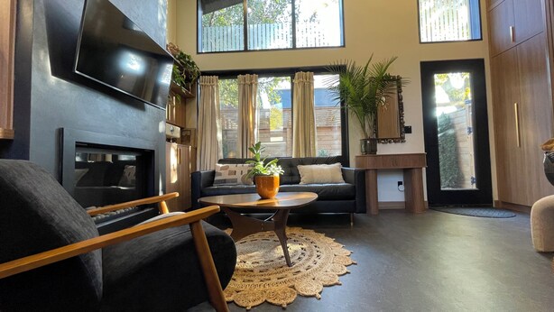 A modern living room with a fireplace, a flat-screen TV, a sofa, a coffee table, and a large window with curtains. - The Roncy Den ~a boutique laneway house (Toronto)
