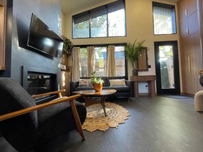 A modern living room with a fireplace, a flat-screen TV, a sofa, a coffee table, and a large window with curtains.