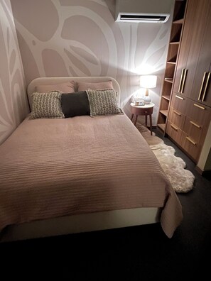 A bedroom with a bed, pillows, a nightstand with a lamp, a wardrobe, and a fur rug. - The Roncy Den ~a boutique laneway house (Toronto)
