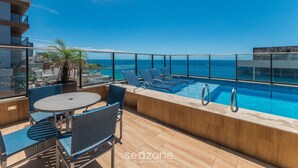 A rooftop pool area with lounge chairs, a table, and a view of the ocean. - Apts 120 m From Barra Beach With Pool and gym in the Building - Esbs (Salvador)