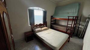 Un dormitorio con una cama individual, una mesita de noche, una ventana con contraventanas y una cama litera.