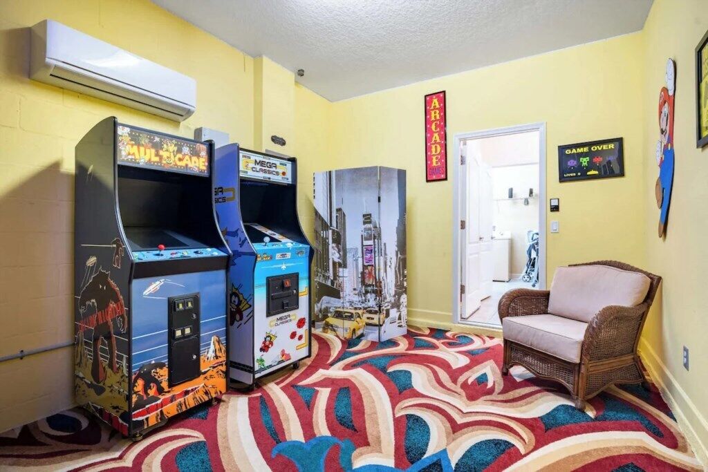 A room with arcade machines, a wicker chair, and a patterned carpet.