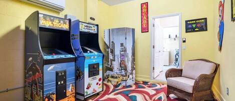 A room with arcade machines, a wicker chair, and a patterned carpet.