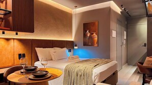 Quarto de hotel moderno com cama, mesa de cabeceira e um espaço de refeições com mesa e cadeiras.