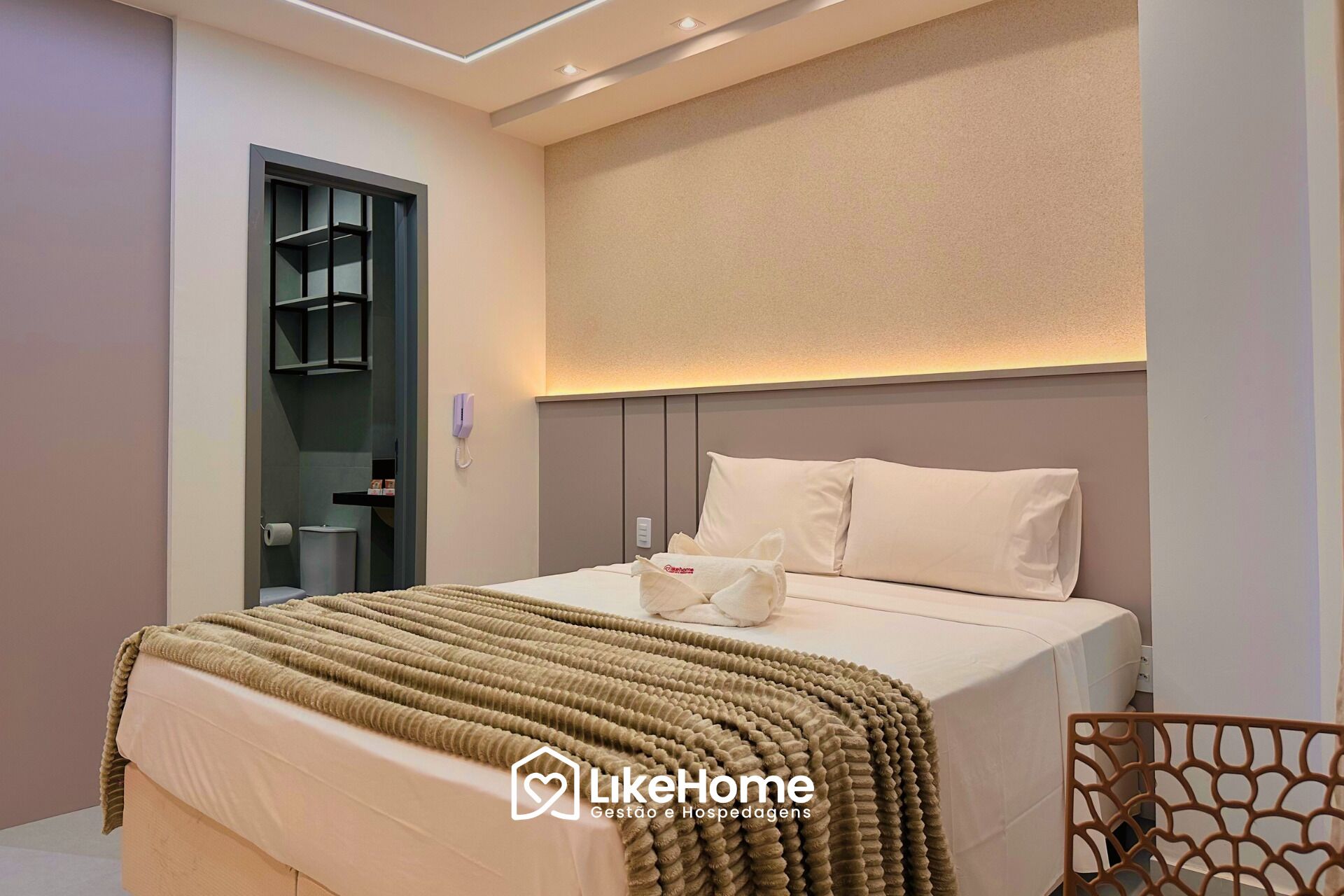 Una habitación de hotel moderna con una cama, un teléfono en la mesita de noche y un baño visible a través de una puerta abierta.