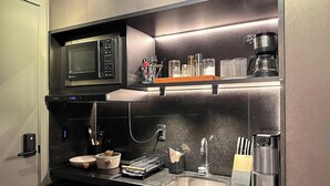 Cozinha compacta com micro-ondas, cafeteira e uma estante com copos.