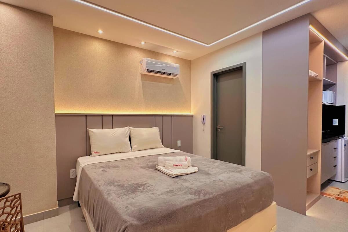 Quarto de hotel com uma cama, mesa de cabeceira e escrivaninha com cadeira.