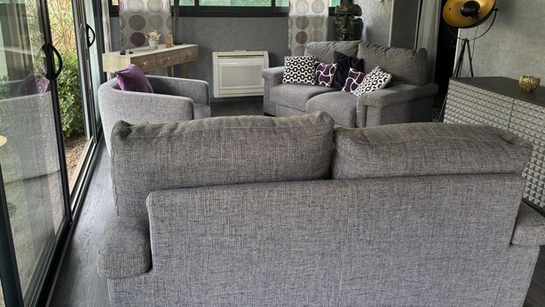 A modern living room with a grey sofa set, patterned cushions, a small side table, and a decorative wall piece.