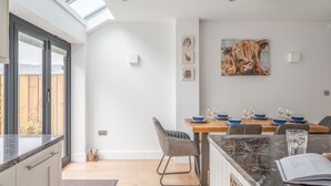 Een moderne keuken met een groot kookeiland, een eethoek met een tafel voor vier personen, en een dakraam boven de keuken.