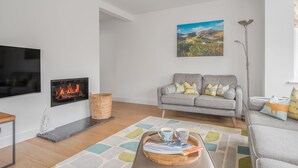 Een moderne woonkamer met een open haard, een grijze bank en een schilderij van een landschap.