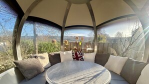 Een ronde tafel met een geribbelde tafelkleed, omringd door zachte zitplaatsen met verschillende kussens, waaronder een kussen met het Union Jack.