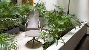 A small, enclosed patio area with a round table and a perforated metal chair, surrounded by various potted plants and a large avocado-themed painting on the wall. - Centro Playa Del Carmen Duna  508 (Playa del Carmen)