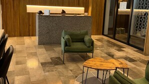 A reception area with a wooden wall, a reception desk, a green armchair, a small wooden table, and a check-in counter. - Centro Playa Del Carmen Duna  508 (Playa del Carmen)