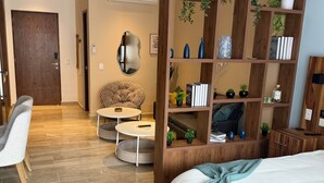 A modern bedroom with a bed, a round coffee table, a sofa, and a wooden bookshelf with plants and books. - Centro Playa Del Carmen Duna  508 (Playa del Carmen)