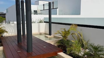 A modern outdoor pool area with wooden decking, a pergola, and various tropical plants.