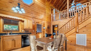 Ein Interieur einer Holzhütte mit Essbereich, Küche und einer Treppe zu einer oberen Ebene.