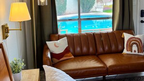 Et hotelværelse med seng, en lædersofa i brunt, udsigt til en swimmingpool og en lampe.