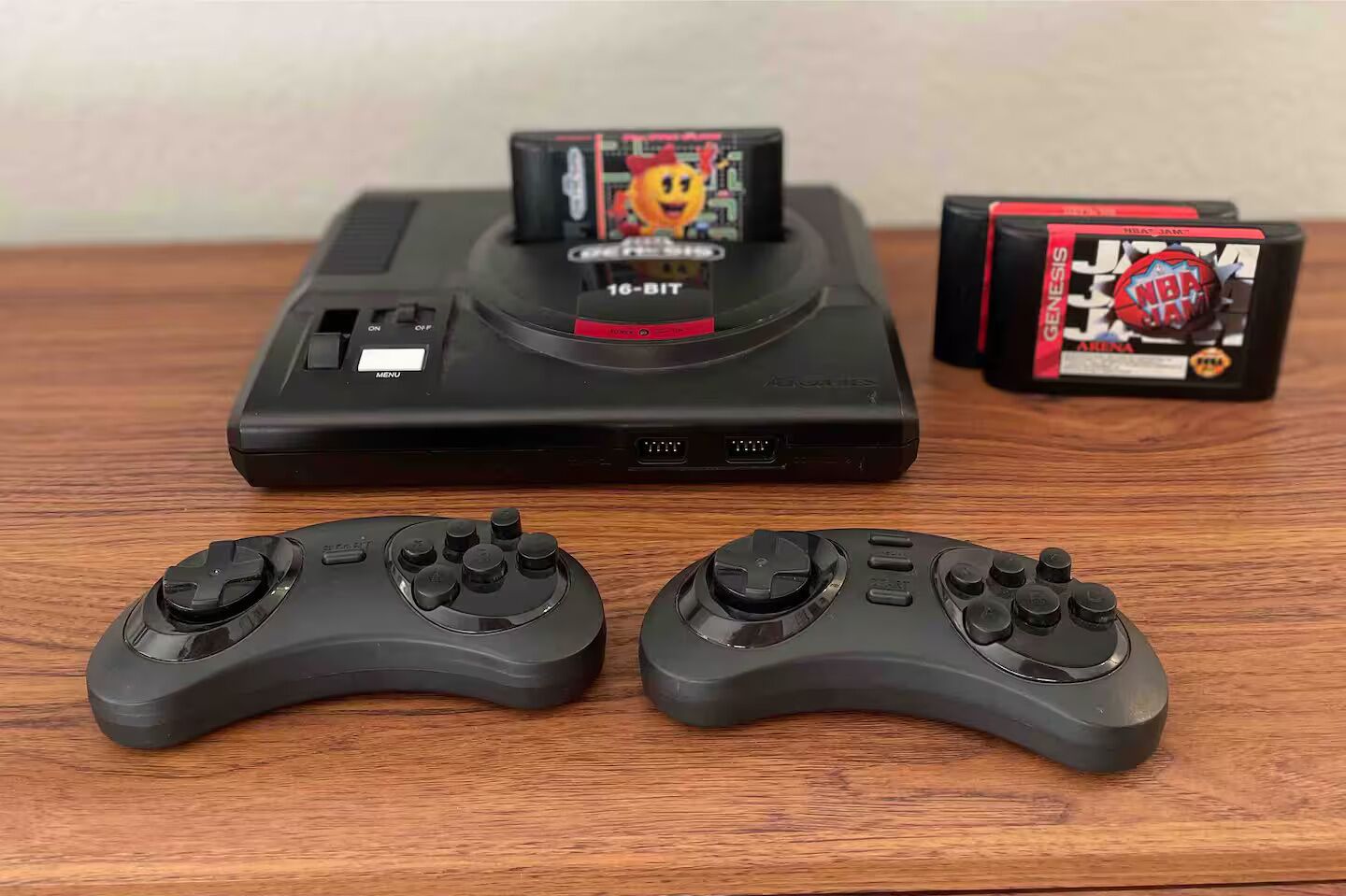 Um console PlayStation 2 com dois controles e duas embalagens de jogos sobre uma superfície de madeira.