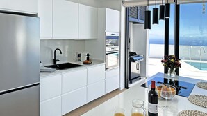 Een moderne keuken met witte kasten, roestvrijstalen apparatuur en uitzicht op een zwembad.