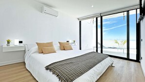 Een moderne slaapkamer met een groot bed, uitzicht op het strand en een klein plankje met een plant.