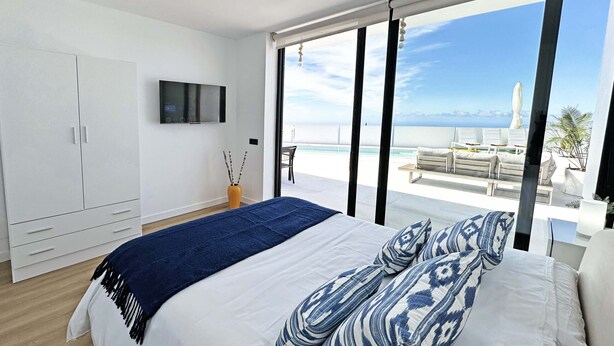 Een slaapkamer met een groot bed, een televisie aan de muur en een balkon met uitzicht op zee.