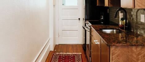 A narrow hallway leading to a kitchen with wooden cabinets, a microwave, and a stainless steel sink.