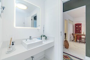 Ein modernes Badezimmer mit einem weißen Waschtisch, einem großen Spiegel und einer Dusche.
