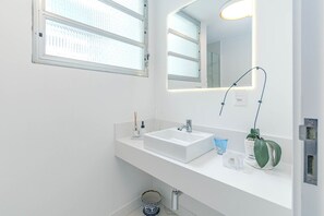 Ein modernes Badezimmer mit einem weißen Waschbecken, einem Spiegel und einer Zimmerpflanze auf der Ablagefläche.