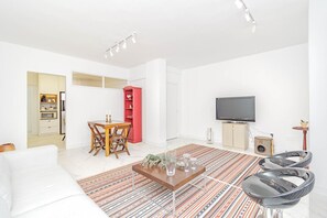 Ein modernes Wohnzimmer mit einem weißen Sofa, einem Holztisch, einem gestreiften Teppich, einem roten Bücherregal, einem Fernseher und einer Katzenkralle.