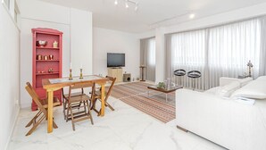 Een moderne woonkamer met een witte bank, een eettafel met stoelen, een rode boekenkast, een flatscreen-tv en een kamerkleed met dessin.