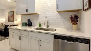 Una cucina moderna con mobili bianchi, un lavandino in acciaio inossidabile e una lavastoviglie.