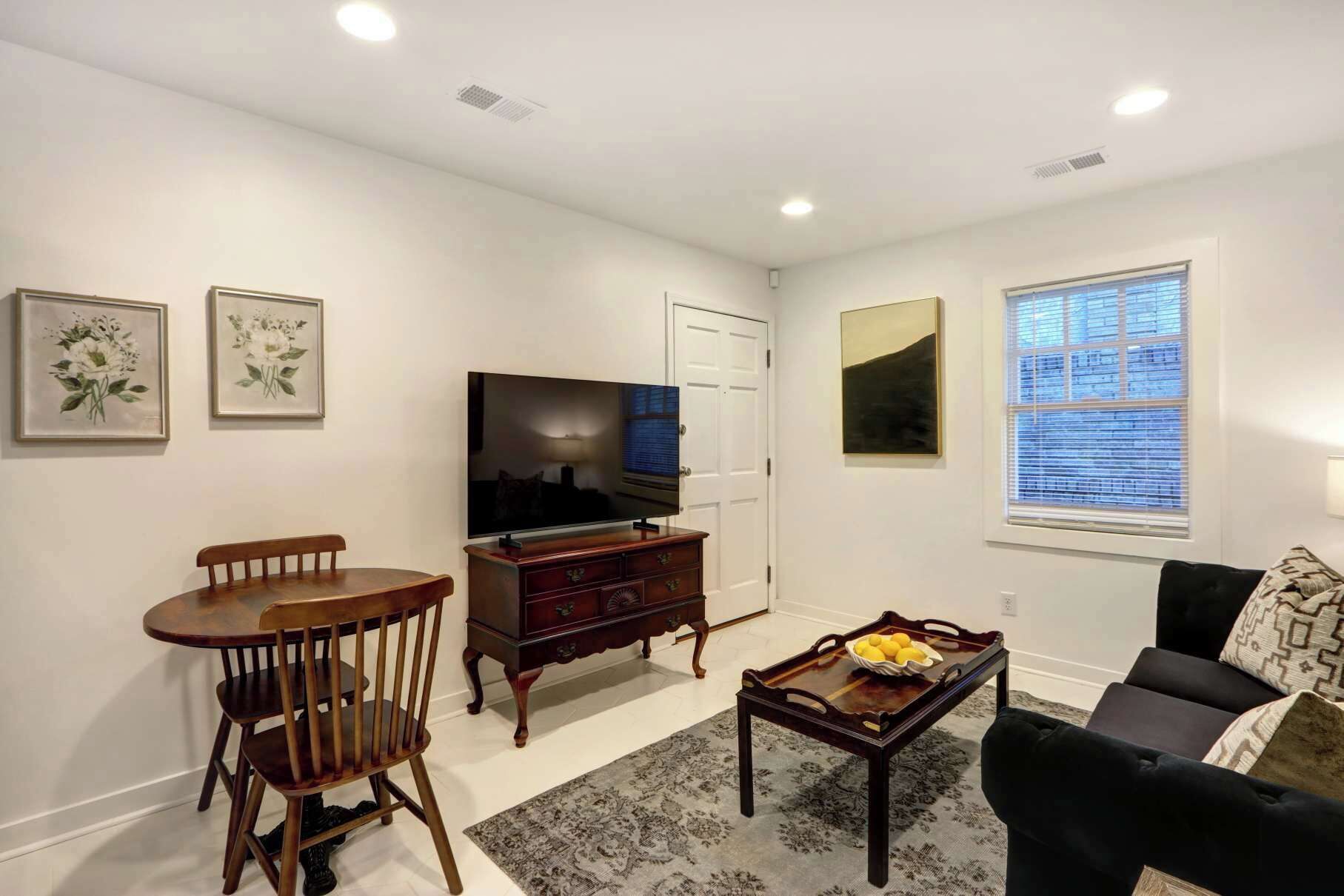 A living room with a TV, wooden furniture, a dining table, and artwork on the walls.