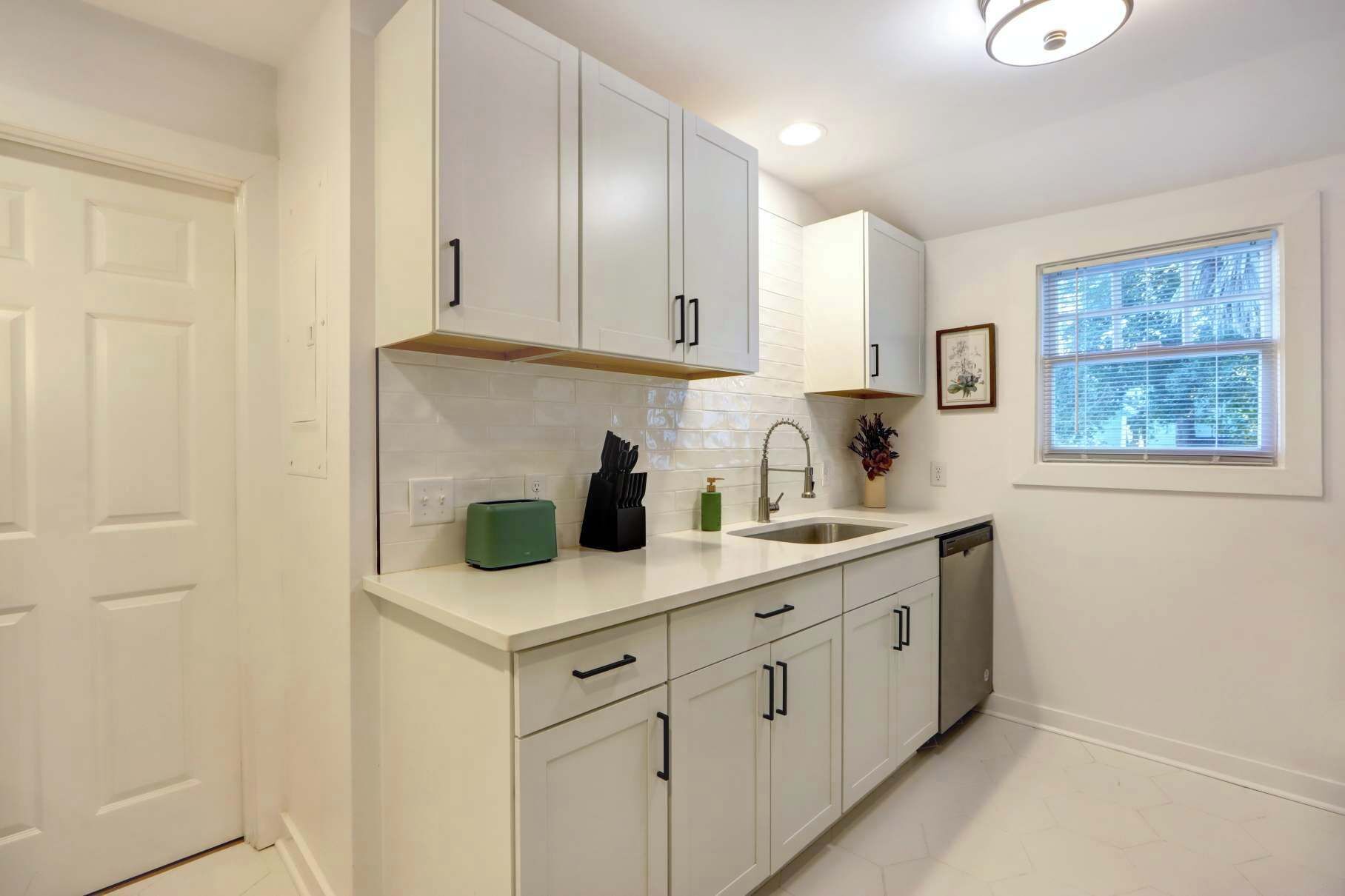 A modern kitchen with white cabinetry, a built-in oven, and a window with blinds.
