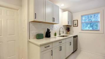 A modern kitchen with white cabinetry, a built-in oven, and a window with blinds.
