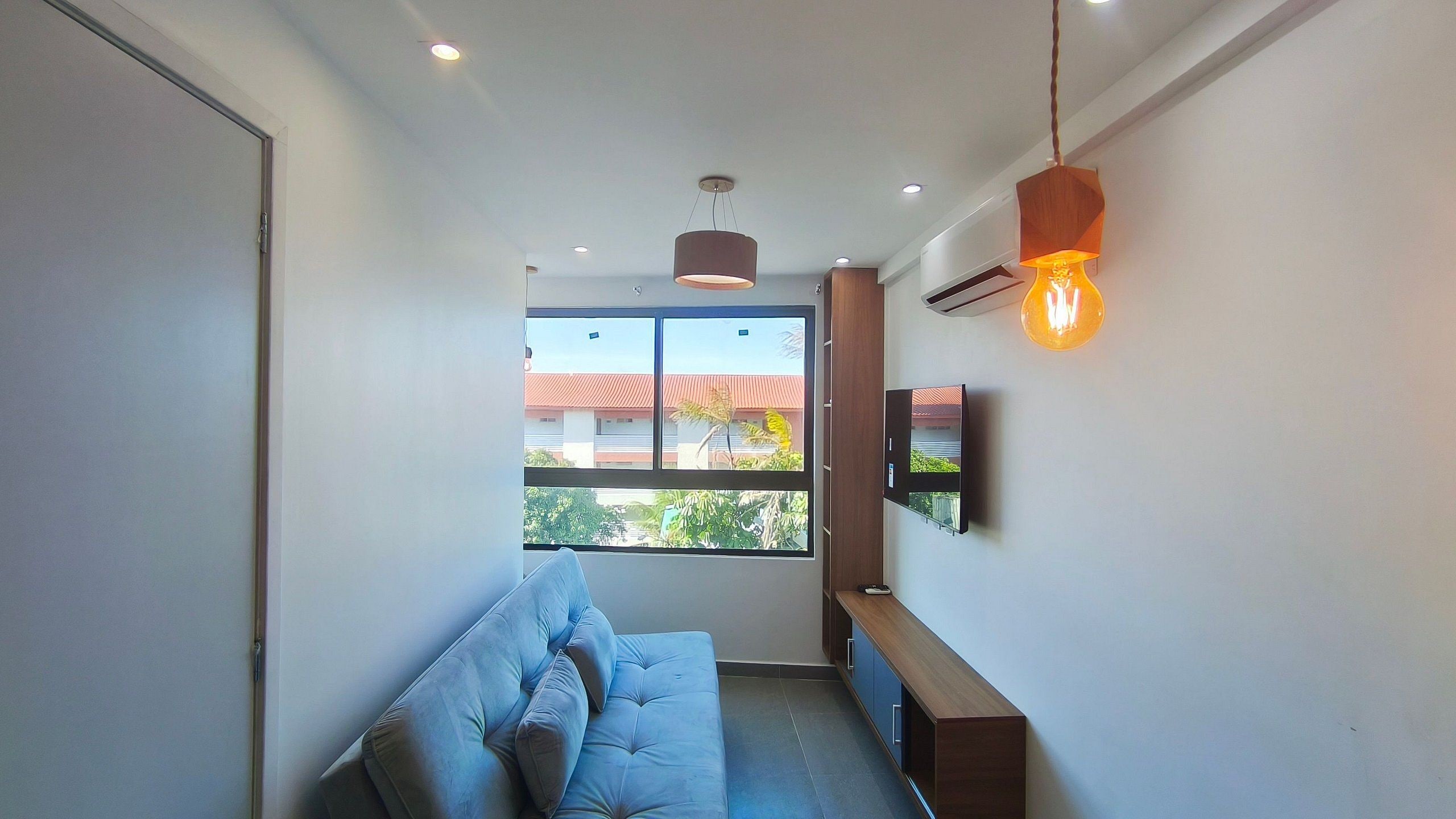 A modern room with a sofa, a TV, and a window with a view of buildings and trees.