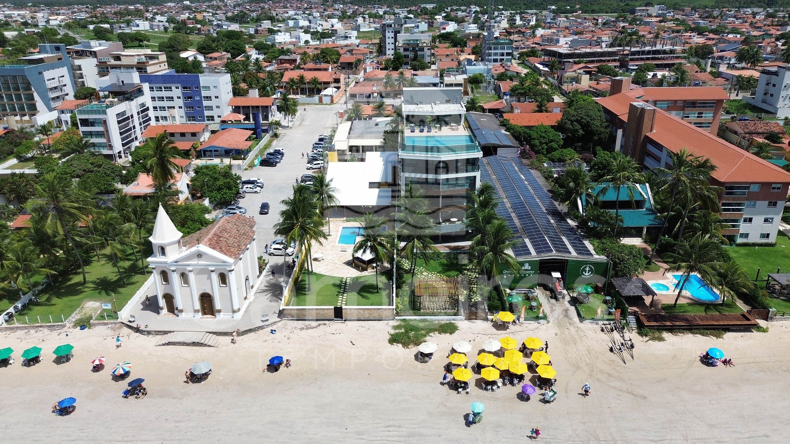 Une ville côtière qui se distingue par son église imposante, un hôtel doté de panneaux solaires et une plage aménagée avec des parasols.