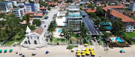 A coastal town with a prominent church, a hotel with solar panels, and a beach area with umbrellas.