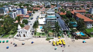 Μια παραθαλάσσια πόλη με μια επιβλητική εκκλησία, ένα ξενοδοχείο με ηλιακούς συλλέκτες και μια παραλία με ομπρέλες.